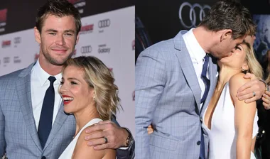 Couple smiling and embracing on a red carpet; both wearing formal attire.