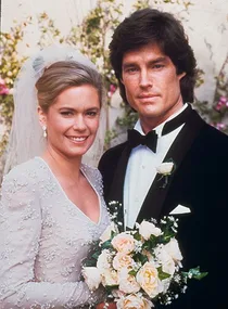A bride and groom, both smiling. The bride holds a bouquet of flowers.