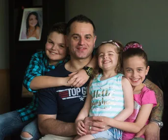 Father with two daughters and a son, smiling on a couch; family photo.