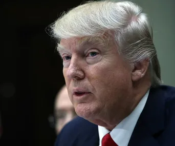 A man in a suit with white hair looks off-camera against a dark background.