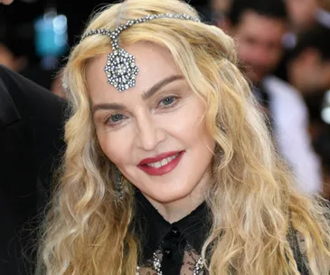 A person with long blonde hair and jeweled headpiece smiles at an event.
