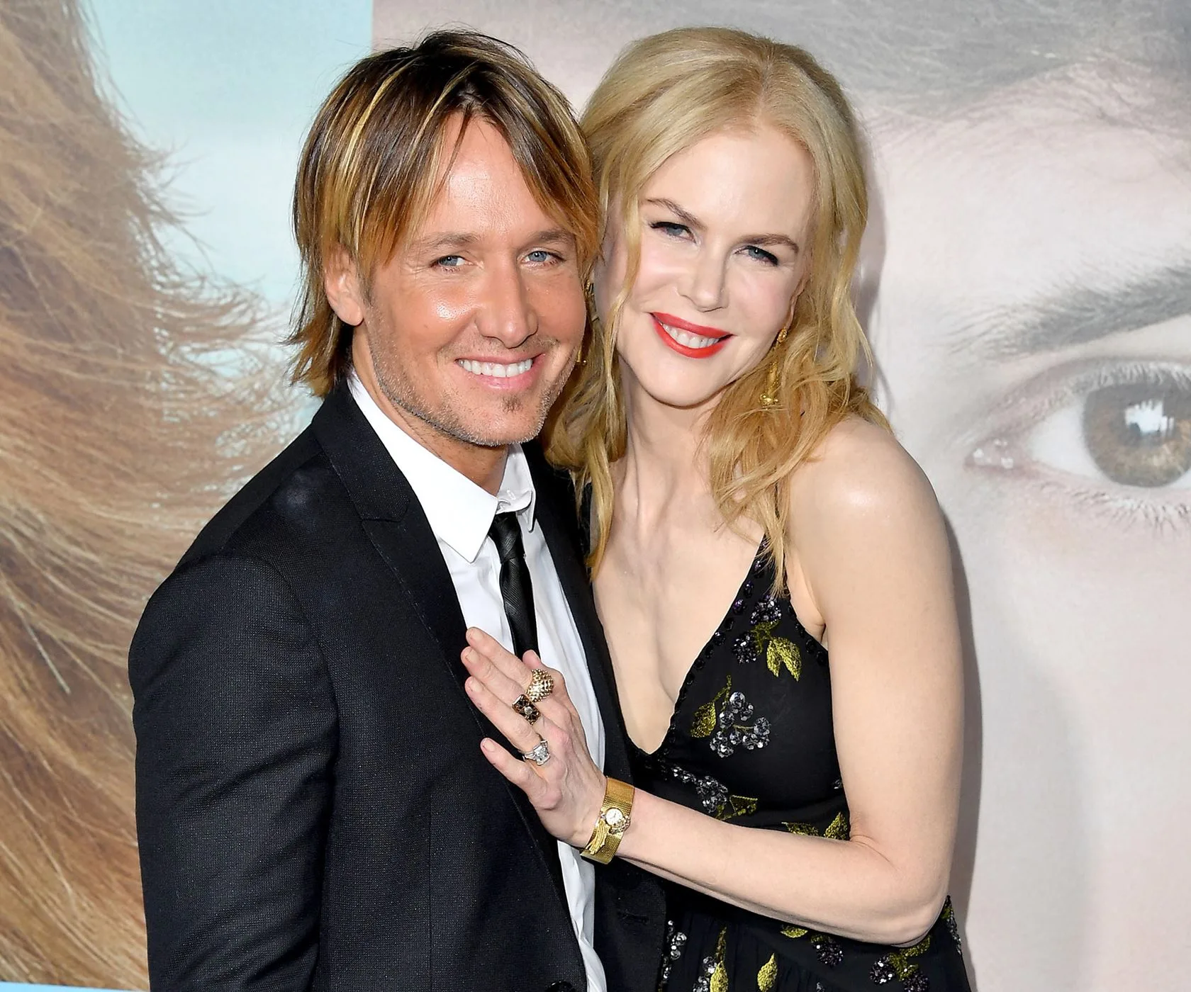 A couple smiling, dressed formally, at a red carpet event.