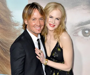 A couple smiling, dressed formally, at a red carpet event.