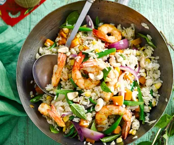 A pan of shrimp fried rice with vegetables, garnished with cashews and fresh herbs.