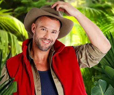 Man in a red vest and hat smiling in a jungle setting.