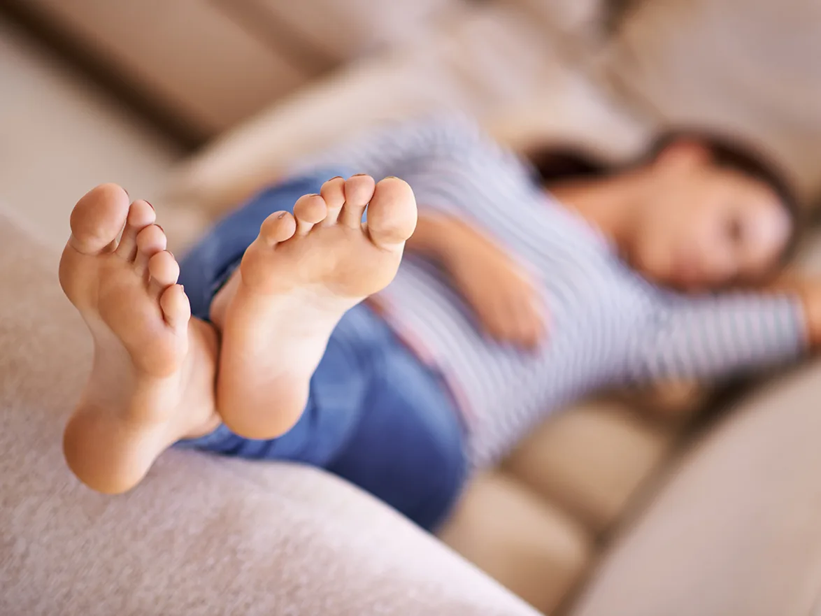 A person lying on a couch with feet in focus, wearing jeans and a striped shirt.