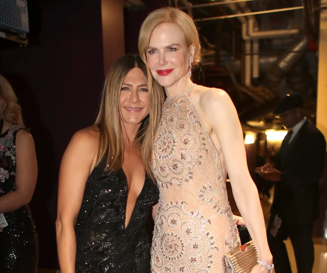 Two women in formal dresses pose together, smiling, at an indoor event with dim lighting.