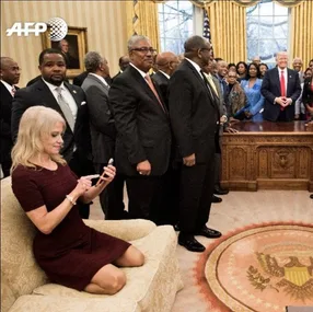 Kellyanne Conway on Oval Office couch during meeting with standing guests and man near Resolute Desk.