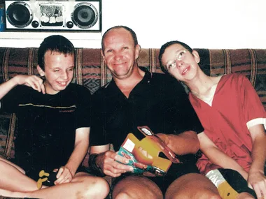Three people sitting on a couch, smiling and posing for a photo; two children and an adult holding a box.