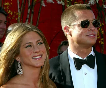 A couple smiling at a formal event, woman with earrings and man in sunglasses and tuxedo.