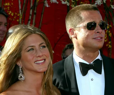 A couple smiling at a formal event, woman with earrings and man in sunglasses and tuxedo.