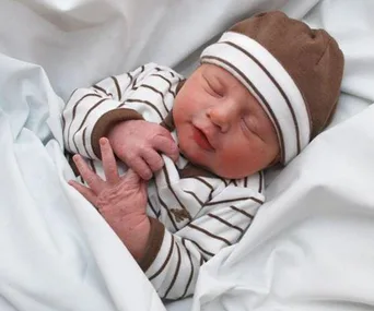 Newborn baby in striped outfit and hat, sleeping peacefully on a white blanket.