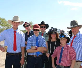 Group of people outdoors in hats, sunglasses, and colorful ties, with trees and clear sky in the background.