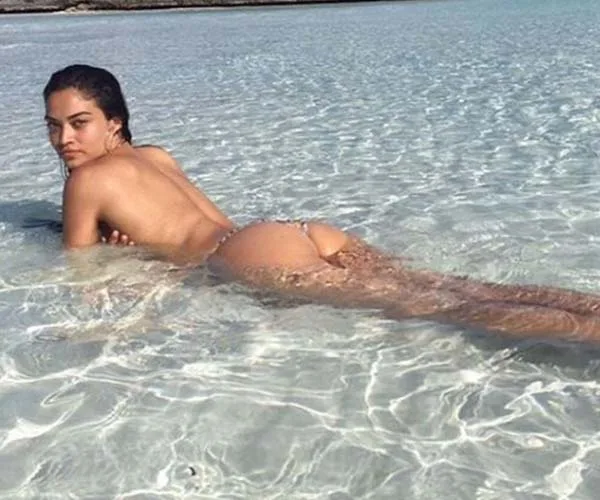 Model posing in clear, shallow seawater, wearing a bikini bottom and facing the camera.