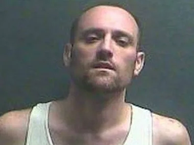Mugshot of an unidentified man with short hair and a beard, wearing a white tank top against a plain background.