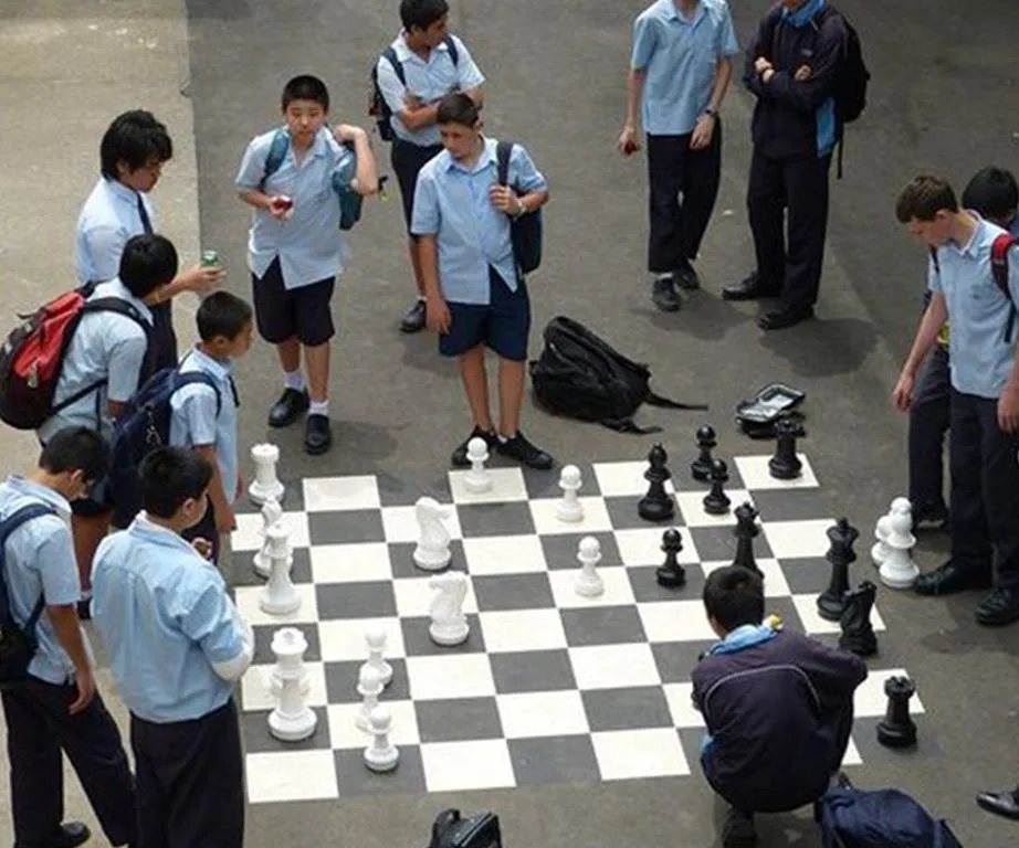 Students in uniforms play and watch a large chess game on a schoolyard.