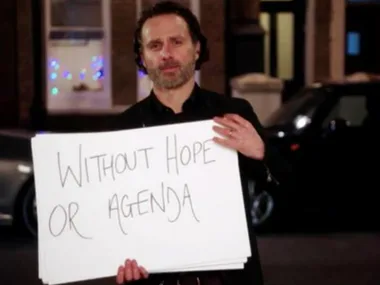 A man holding a sign that reads "Without Hope or Agenda" from a scene reminiscent of "Love Actually."