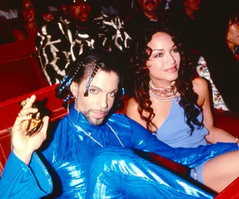A man in a blue outfit sits next to a woman in a blue dress, attending an event.