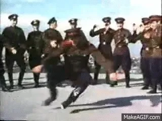 Group of uniformed soldiers watching a man in military attire perform a traditional dance energetically.