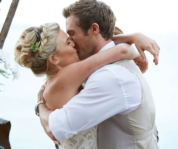 Couple sharing a kiss at their beach wedding, embracing each other lovingly.