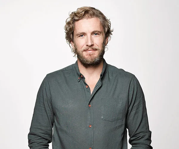 Man with curly hair and beard in a green shirt, standing against a plain white background.
