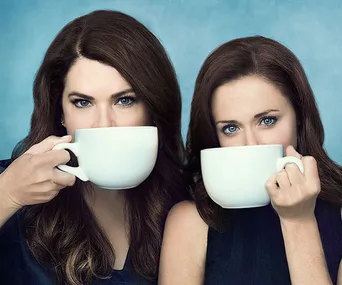Two women holding large coffee mugs, facing forward with a soft blue background.