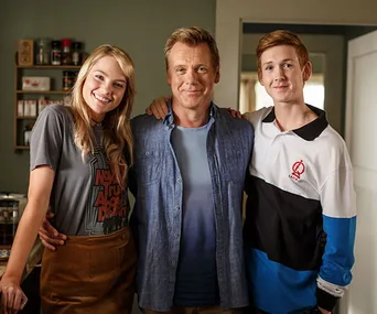 Family from "800 Words" TV show smiling, with the father in the center, daughter on the left, and son on the right in their home.
