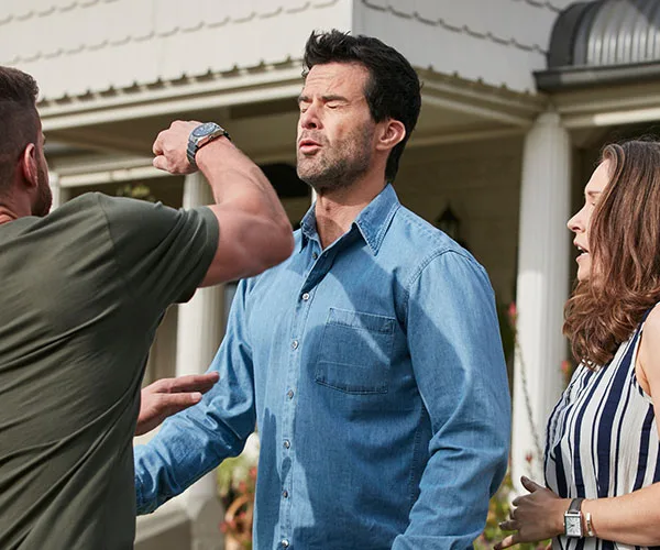 A tense confrontation outside a house; two men argue as a woman looks on.
