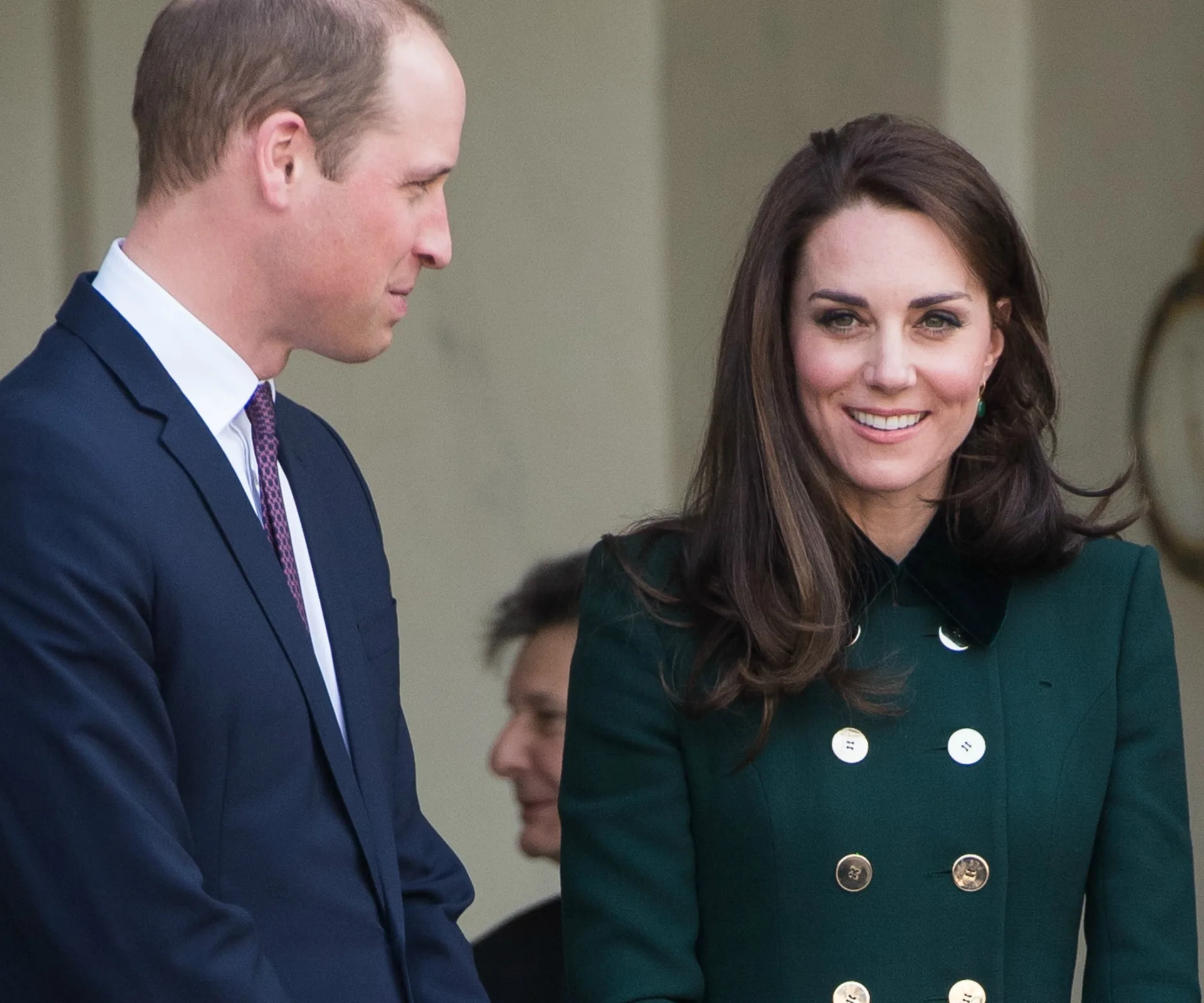 The Duke and Duchess of Cambridge smiling during a visit, he in a suit, she in a green coat.