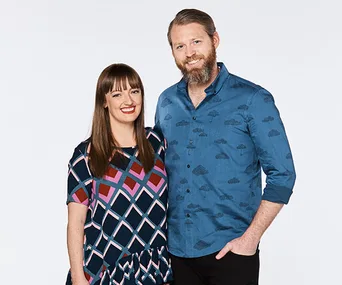 Man and woman smiling, posing together; woman in patterned dress, man in blue shirt with cloud design.