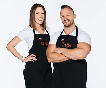 Two "My Kitchen Rules" contestants wearing black aprons with the show's logo, smiling and posing against a white background.