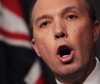 Close-up of a man speaking with an Australian flag in the background.