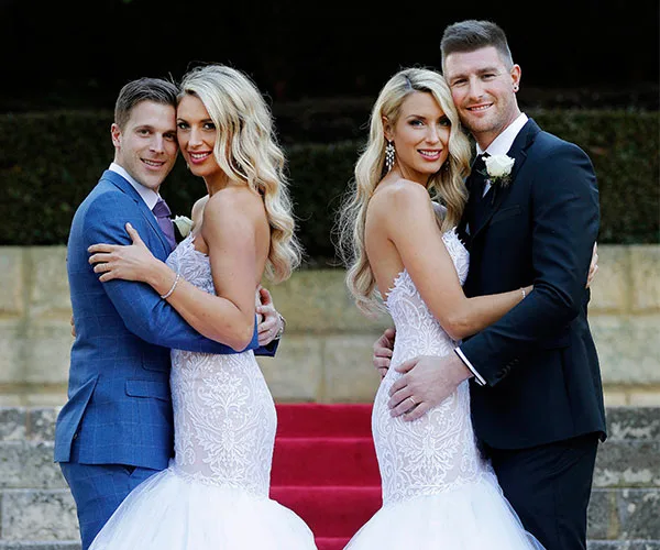 Couples in wedding attire on red carpet from "Married at First Sight." Two women in lace dresses with their grooms.