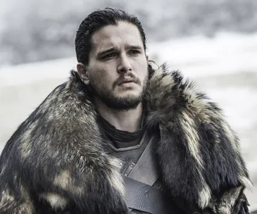 Kit Harington as Jon Snow in "Game of Thrones," wearing a fur cloak, looking pensive outdoors.