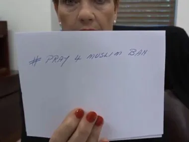 A person holding a sign with the handwritten text "# PRAY 4 MUSLIM BAN."