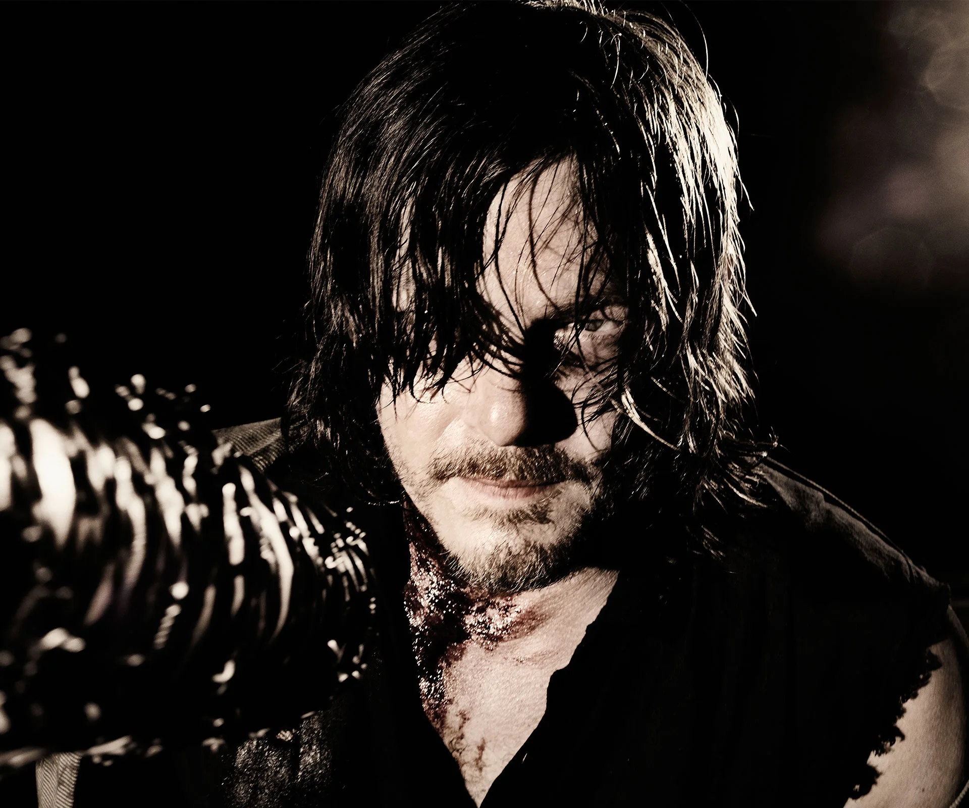 Dark, intense scene featuring a long-haired man with a grim expression, holding a weapon wrapped with barbed wire.