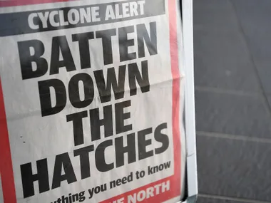 Cyclone alert sign reading "Batten Down the Hatches" in bold letters on a street display.