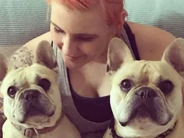 Person cuddling two French Bulldogs, all looking content.