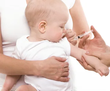 A baby receives a vaccination shot while being gently held by a caregiver.