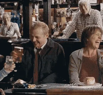 People laughing and clinking glasses in a lively pub setting.