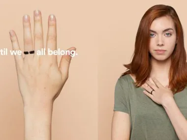 A person wearing a broken black ring on their finger, hand over heart, with text "until we all belong" beside.
