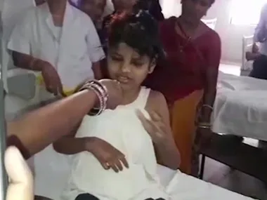 A child sitting on a hospital bed surrounded by adults, with attention focused on someone off-camera.