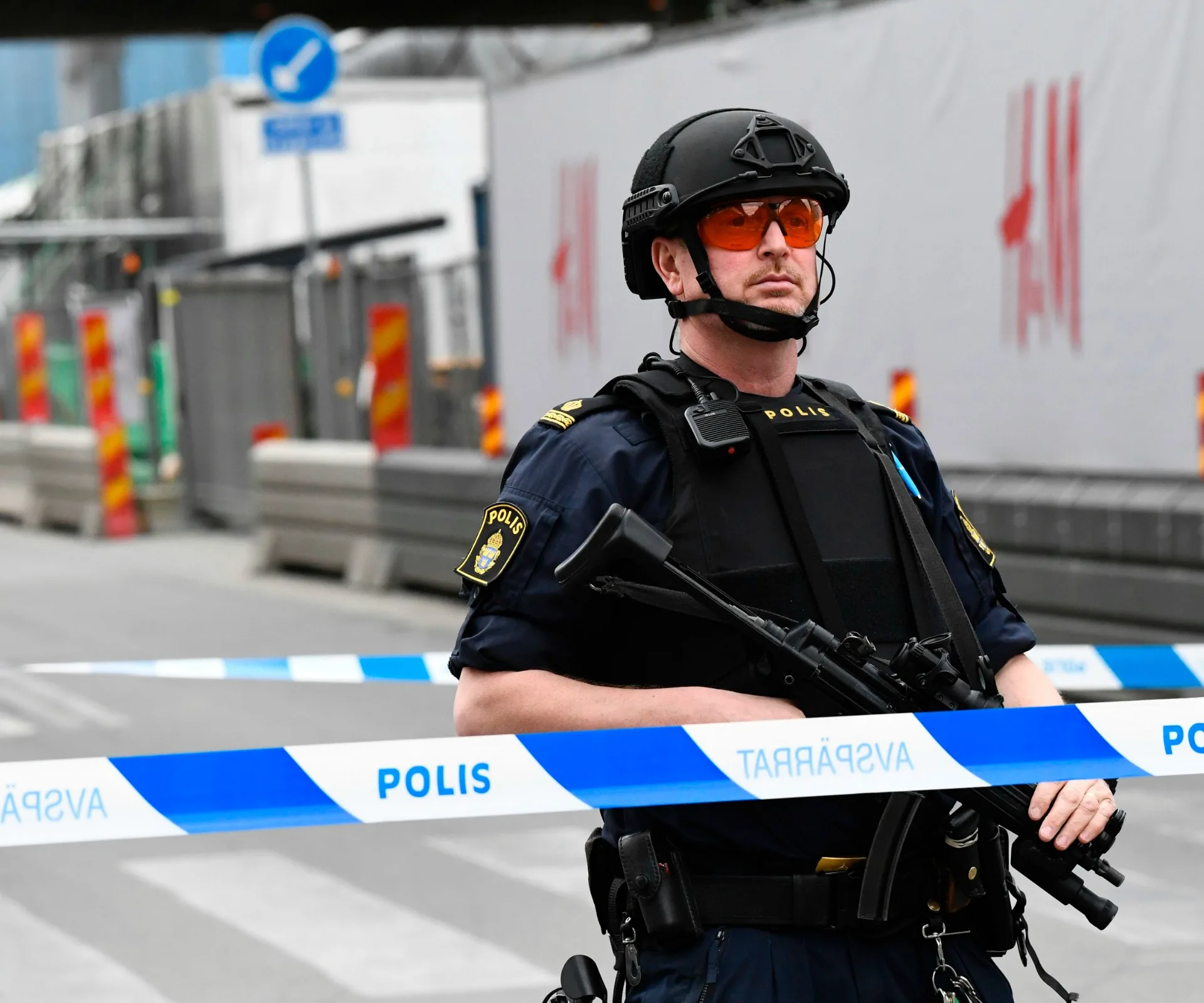 Police officer stands guard with rifle near cordoned-off area in Stockholm after attack.