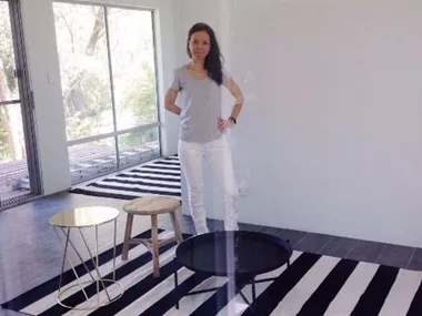 Woman standing in a minimalistic room with striped rug and small tables.