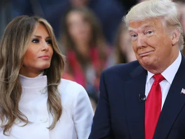 Man and woman in formal attire, woman looking to her left, man with a smirk; crowded background.