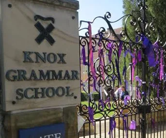 Knox Grammar School sign next to an ornate gate adorned with purple ribbons.