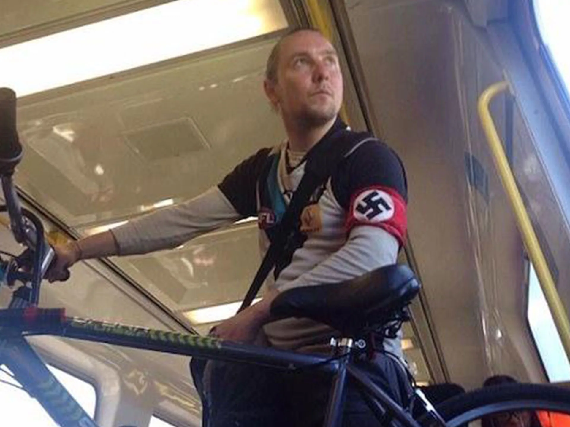Port Adelaide supporter on a train, wearing a jersey and a Nazi swastika armband while holding a bicycle.