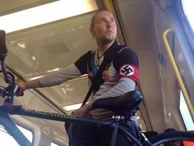 Port Adelaide supporter on a train, wearing a jersey and a Nazi swastika armband while holding a bicycle.