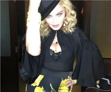 Woman in black outfit and hat posing indoors, wearing yellow bracelets and floral skirt.