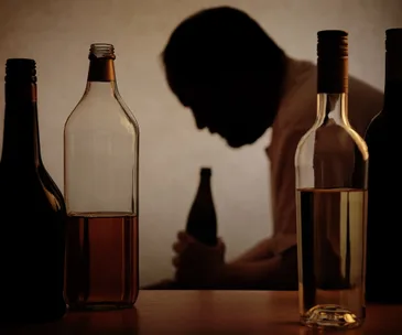 Silhouette of a person holding a bottle, surrounded by various liquor bottles on a table.